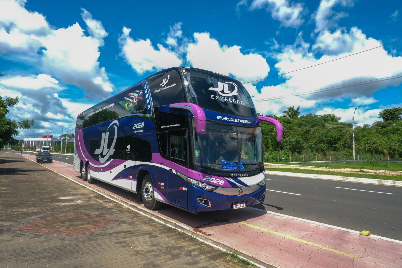 Ônibus leito de dois andares da JL Expresso, pintura roxa e azul, parado à beira da estrada em dia ensolarado