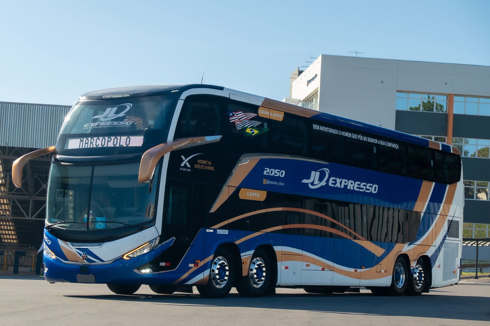 Ônibus leito de dois andares da JL Expresso, modelo Marcopolo, estacionado em frente à garagem sob céu azul
